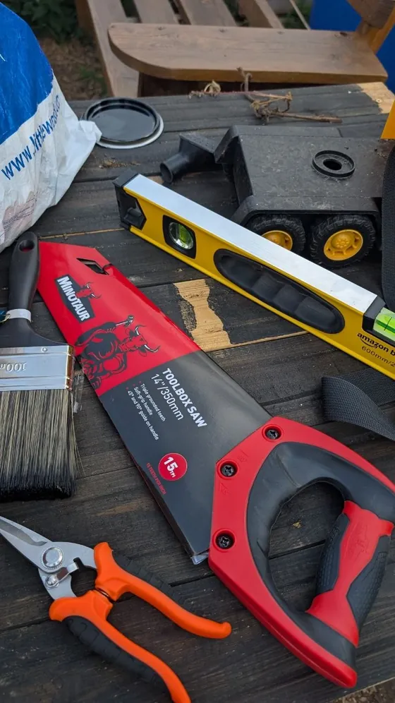 A hand saw, a spirit level and other tools laid out on a wooden table